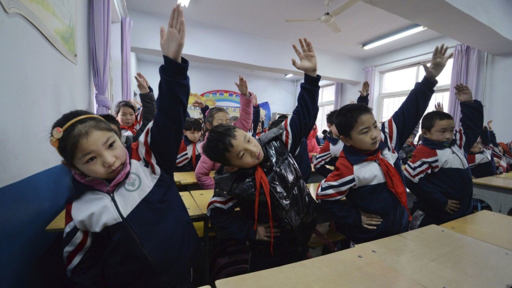 Primary school students practise morning exercises during class break in a classroom on a hazy day in Handan