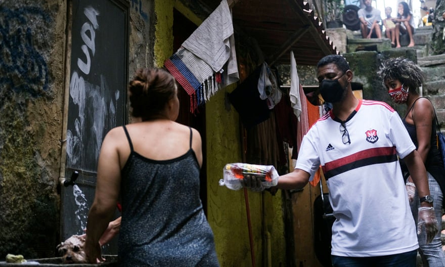 Лидер общины Уильям да Росинья, одетый в защитную маску и перчатки, на этой неделе доставляет пожертвования жителям поселка Росинья в Рио-де-Жанейро.
